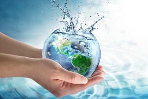 Hands holding a glass bowl with a water splash and a globe inside, symbolizing water conservation and the benefits of tankless water heaters.