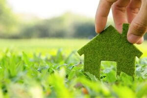 Hand placing a green eco-friendly house symbol on lush grass, representing environmentally conscious home solutions and the importance of sustainability in plumbing.