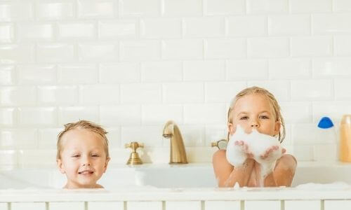 Children playing in a bathtub filled with bubbles, showcasing a relaxing bathroom environment, relevant to bathtub plumbing systems and home comfort.
