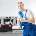 Male plumber in blue overalls holding a pipe wrench in a modern kitchen, showcasing sewer maintenance expertise.
