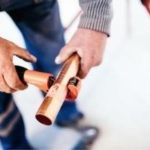 Close-up of hands using a pipe cutter on a copper pipe, featuring plumbing tools by Lodder Brothers Limited.