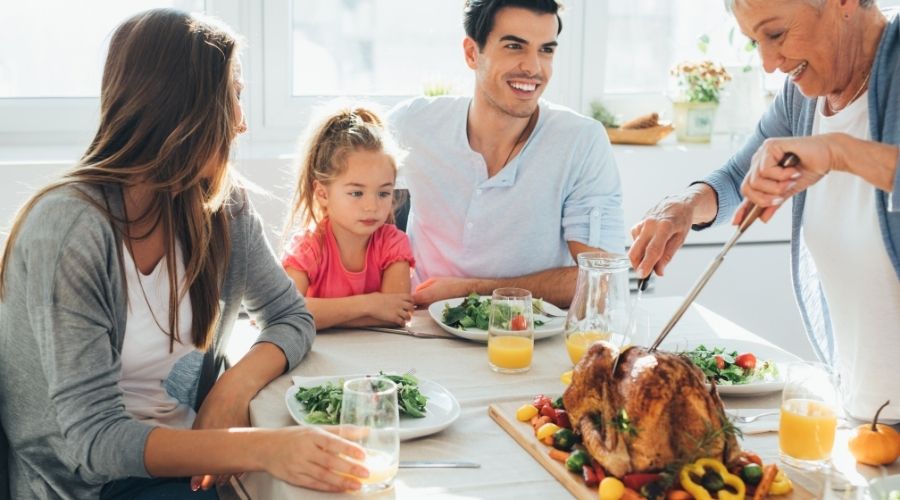 Family gathering around a table enjoying a Thanksgiving dinner, featuring a roasted turkey, fresh salads, and drinks, highlighting the importance of home cooking during the holiday season.