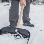 Person shoveling snow with a dark shovel in a winter landscape, highlighting winter plumbing by Lodder Brothers Limited.