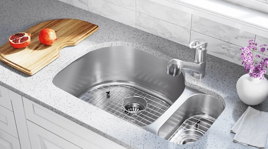 Stainless steel sink in a modern kitchen with a cutting board, pomegranate, and flower vase, showcasing home plumbing care.