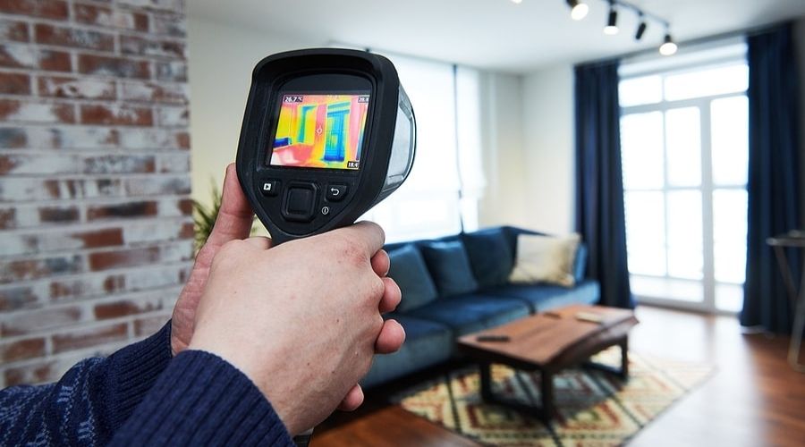 Person holding a thermal camera in a modern living room for plumbing diagnostics.