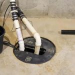 Sump pump installation in a basement, featuring PVC pipes and a collection bucket for effective water management.