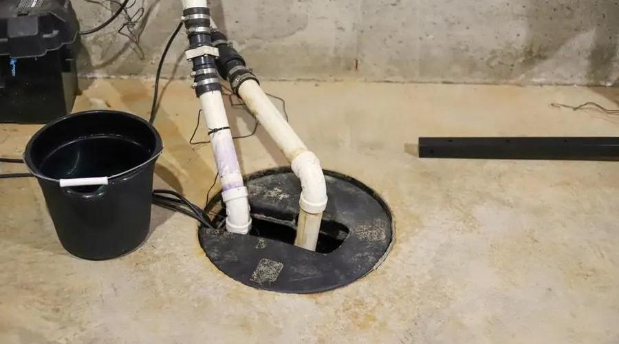 Sump pit and pump system with PVC pipes and black bucket for effective home plumbing maintenance by Lodder Brothers Limited.