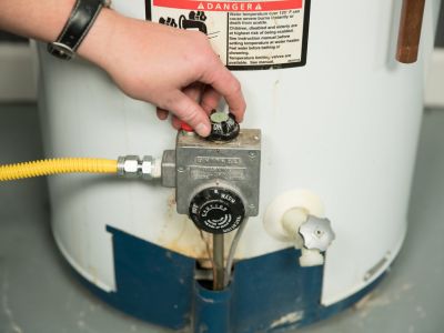 Hand adjusting the valve on a water heater, illustrating the process of shutting off and draining the water heater to prevent leaks and save energy during prolonged absences.