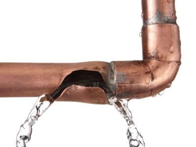 Broken copper pipe leaking water, illustrating plumbing issues and potential water damage risks for homeowners during prolonged absences.