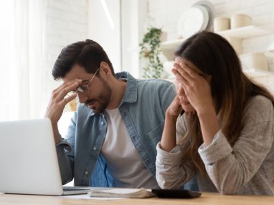 Frustrated couple looking at a laptop, illustrating the stress of high utility costs related to water heater maintenance and efficiency.