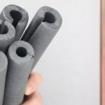 Hand holding dark gray cylindrical foam pieces for plumbing insulation and protection against winter freezing.