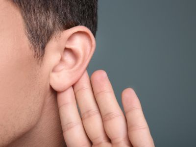 Person listening closely with hand cupped to ear, emphasizing the importance of identifying odd sounds from a water heater.