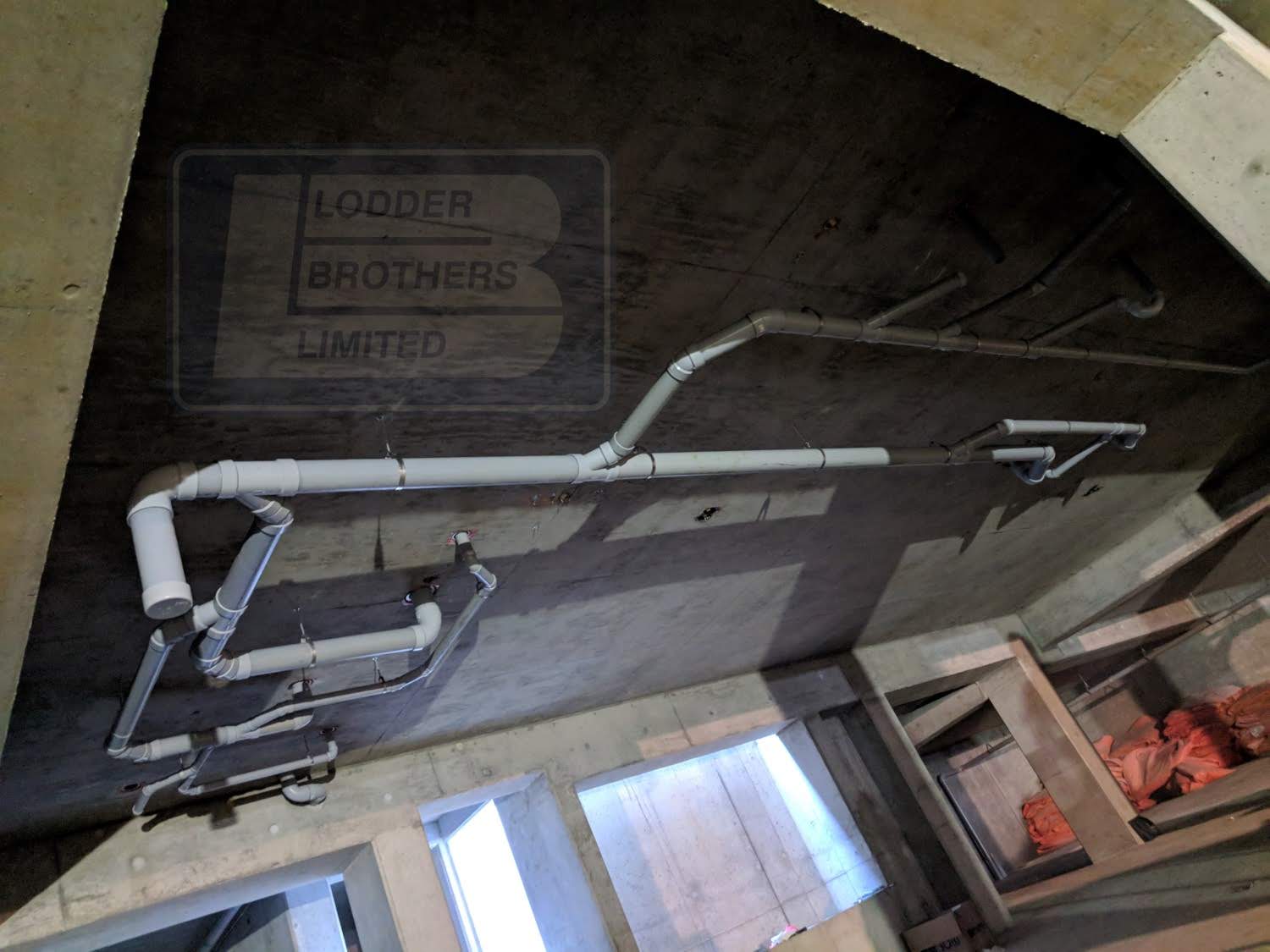 Pipes installed on a concrete ceiling in a new commercial construction site, featuring the Lodder Brothers Limited logo, highlighting plumbing installation services.