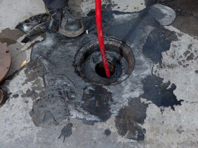Professional plumber using a high-pressure hose in a drain, demonstrating hydro jetting technique to clear tough clogs and buildup.