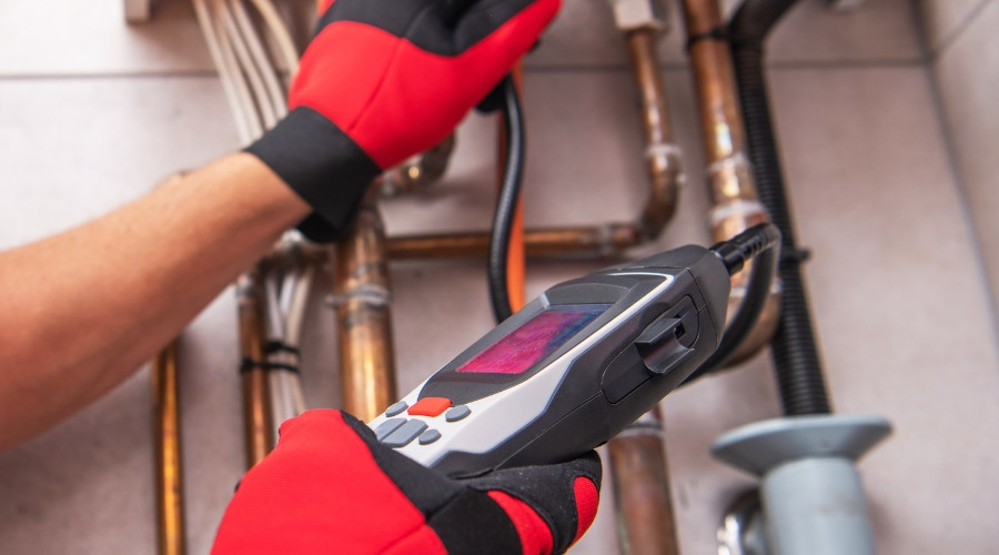 Plumber using gas leak detection device on pipes, emphasizing safety in plumbing services.
