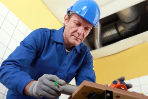 Plumber in blue uniform and hard hat inspecting plumbing system, emphasizing the importance of professional plumbing inspection for new homeowners.
