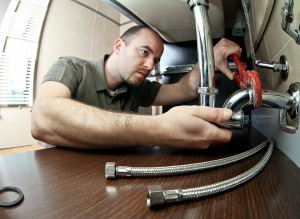 Man using a wrench to repair plumbing under a kitchen sink, showcasing professional plumbing skills relevant to home projects and maintenance.