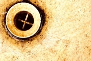 Close-up of a dirty drain with a visible cross pattern, emphasizing plumbing issues related to clogged drains and the risks of chemical cleaners.