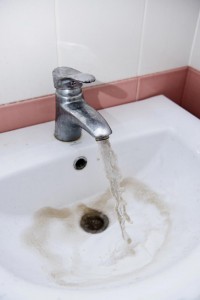 Discolored water flowing from a faucet into a sink, indicating potential plumbing issues and the need for inspection.